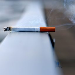 A lit cigarette sitting on a ledge outside.