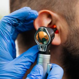 Man gets an ear exam from doctor with otoscope.