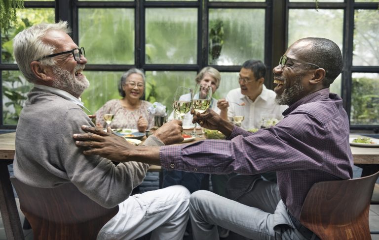 A group of older friends laughing and talking as they enjoy dinner together.