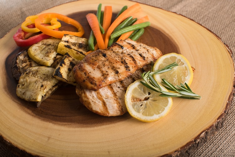 Grilled chicken with vegetables on a wooden dinner plate.